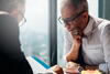 a man wearing glasses sitting at a table looking over a file with another man